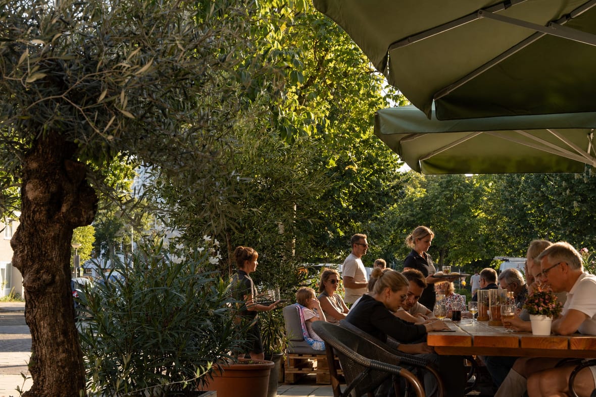 Bediening loopt met borden langs een lange tafel op het terras van Brasserie Lenny in de avondzon