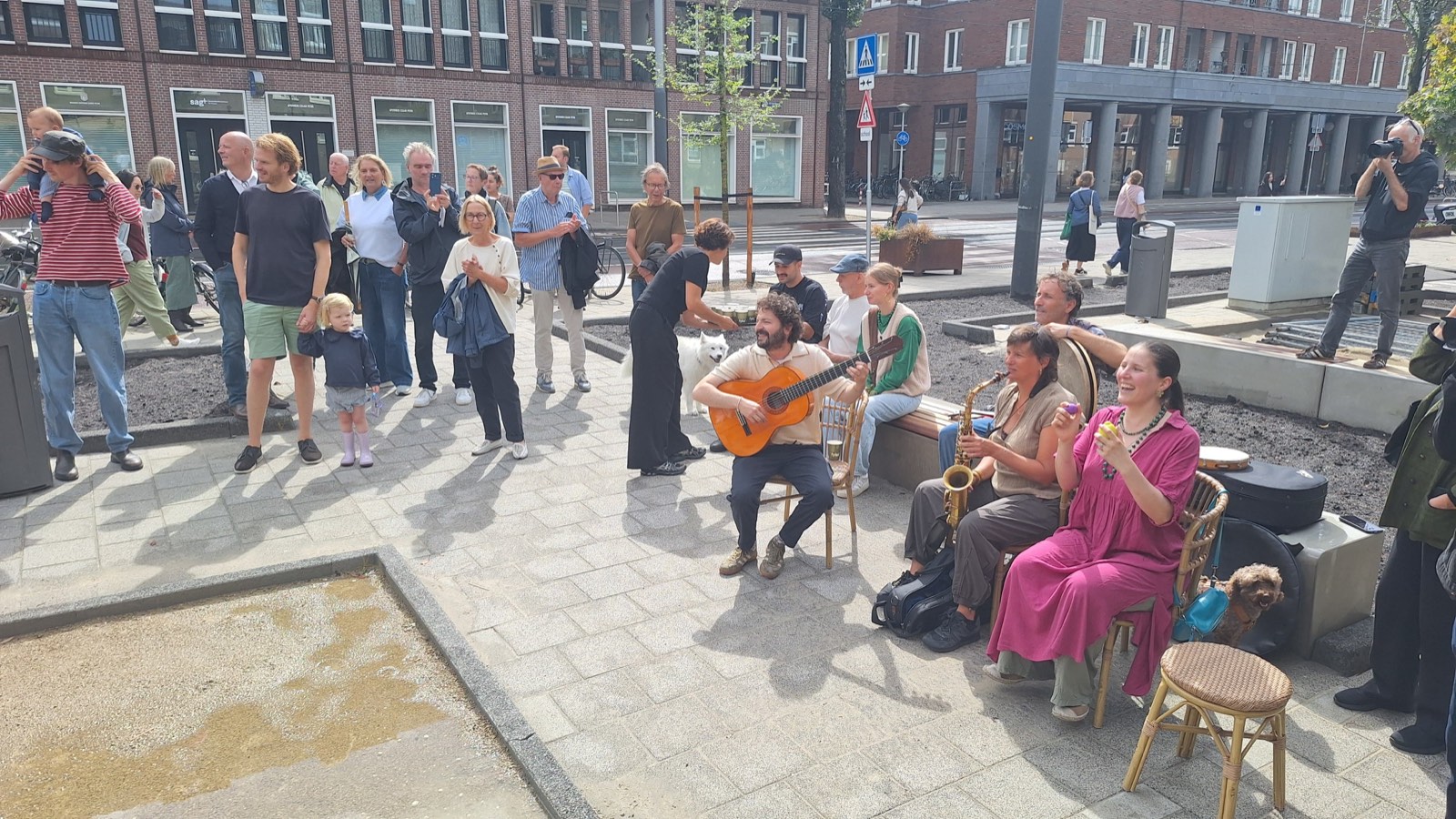 Muzikanten van Casa Guitarra spelen met gitaar, saxofoon en percussie voor een toekijkend publiek op het vernieuwde pleintje