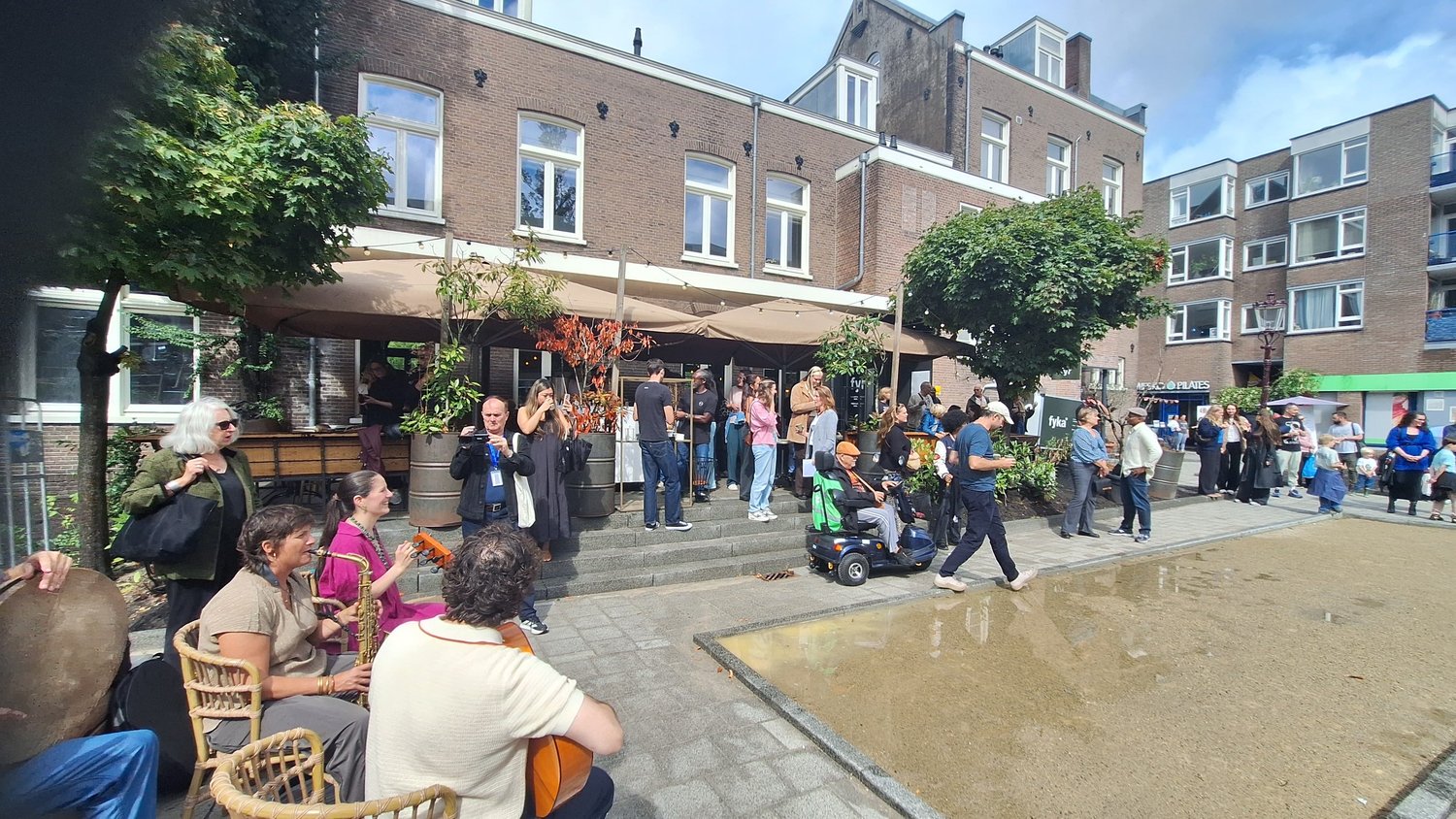 Het nieuwe pleintje bij de 1e Coehoornstraat met de jeu-de-boulesbaan, publiek op de trappen en muzikanten tijdens de opening