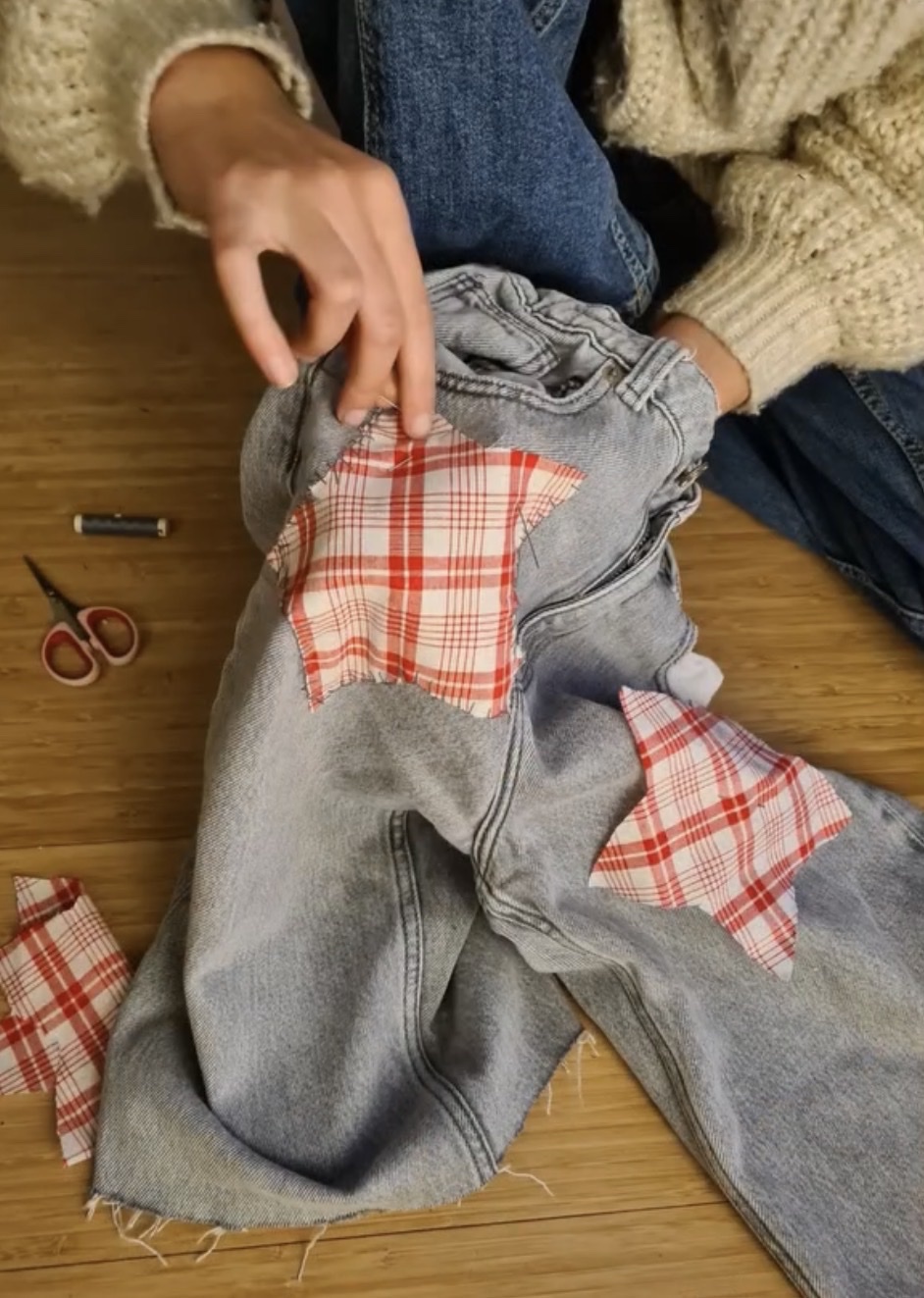 Handen zetten geruite lapjes op een grijze spijkerbroek, met schaar en garen op de vloer
