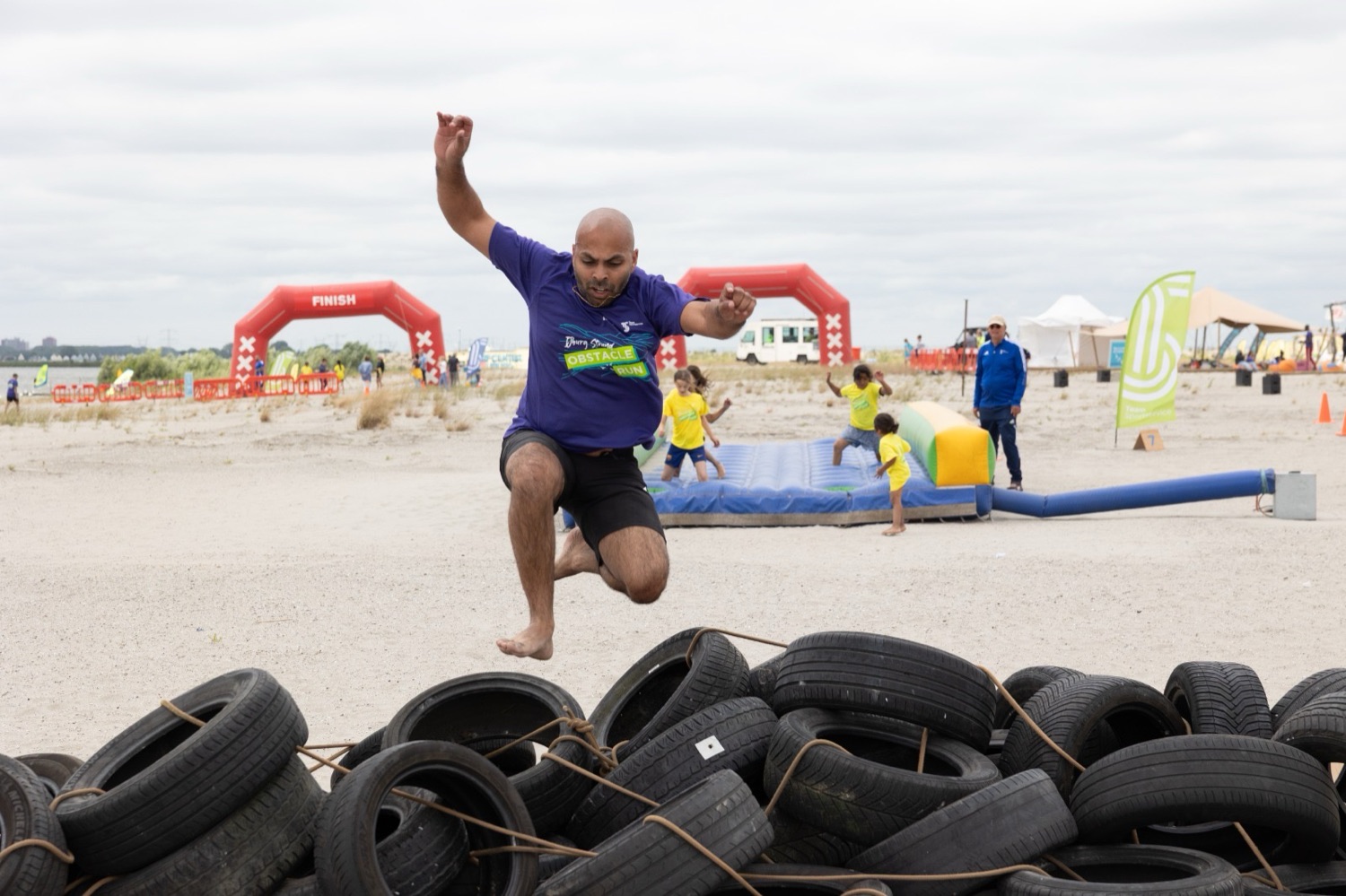 Deelnemer springt over een bandenmuur tijdens de IJburg Strand Obstacle Run