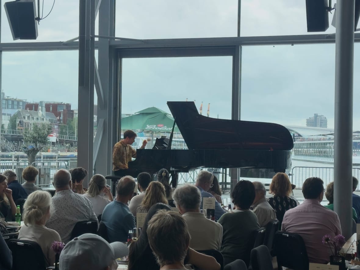 Het publiek luistert in de Entreehal van het Muziekgebouw, met zicht op het IJ door de grote ramen