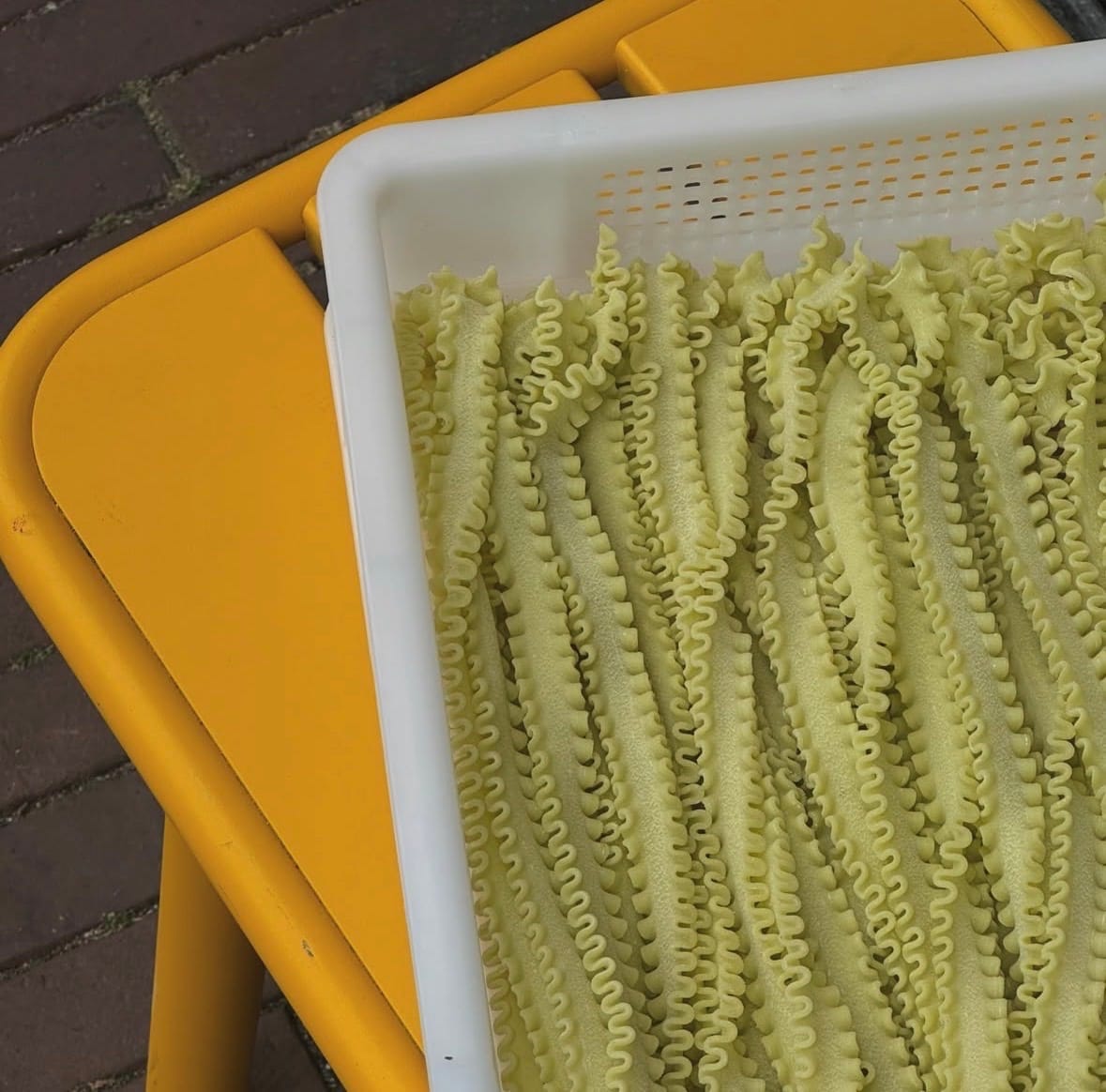 Bakken met vers gedraaide pasta die buiten op een gele stoel liggen te drogen