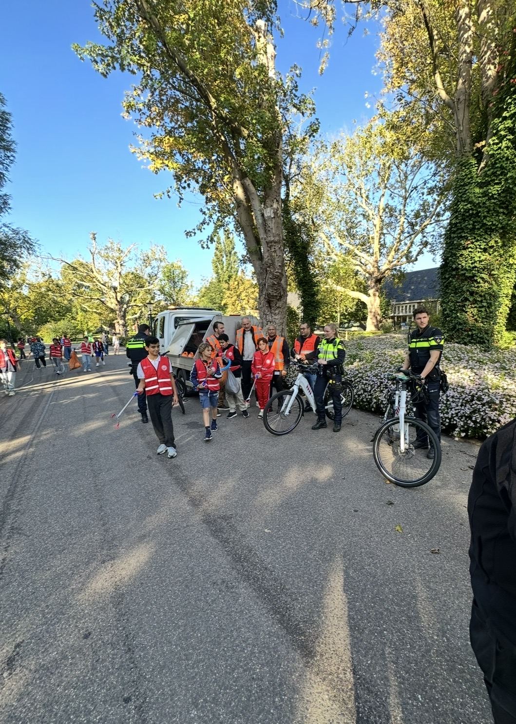 Vrijwilligers in rode hesjes, fietsende handhavers en een gemeentewagen tijdens een opruimactie in het Oosterpark