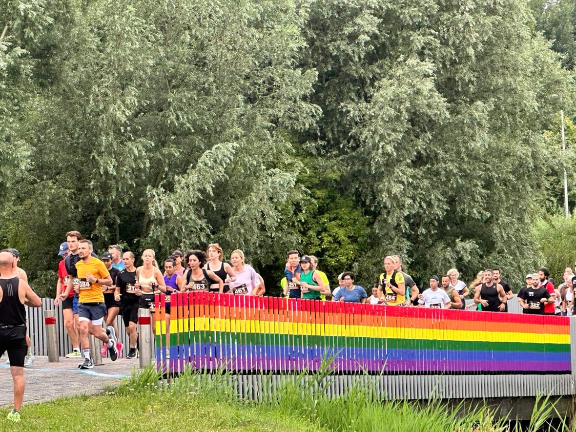 Deelnemers van de Amsterdam Pride Run rennen over een brug met regenboogkleurige leuningen