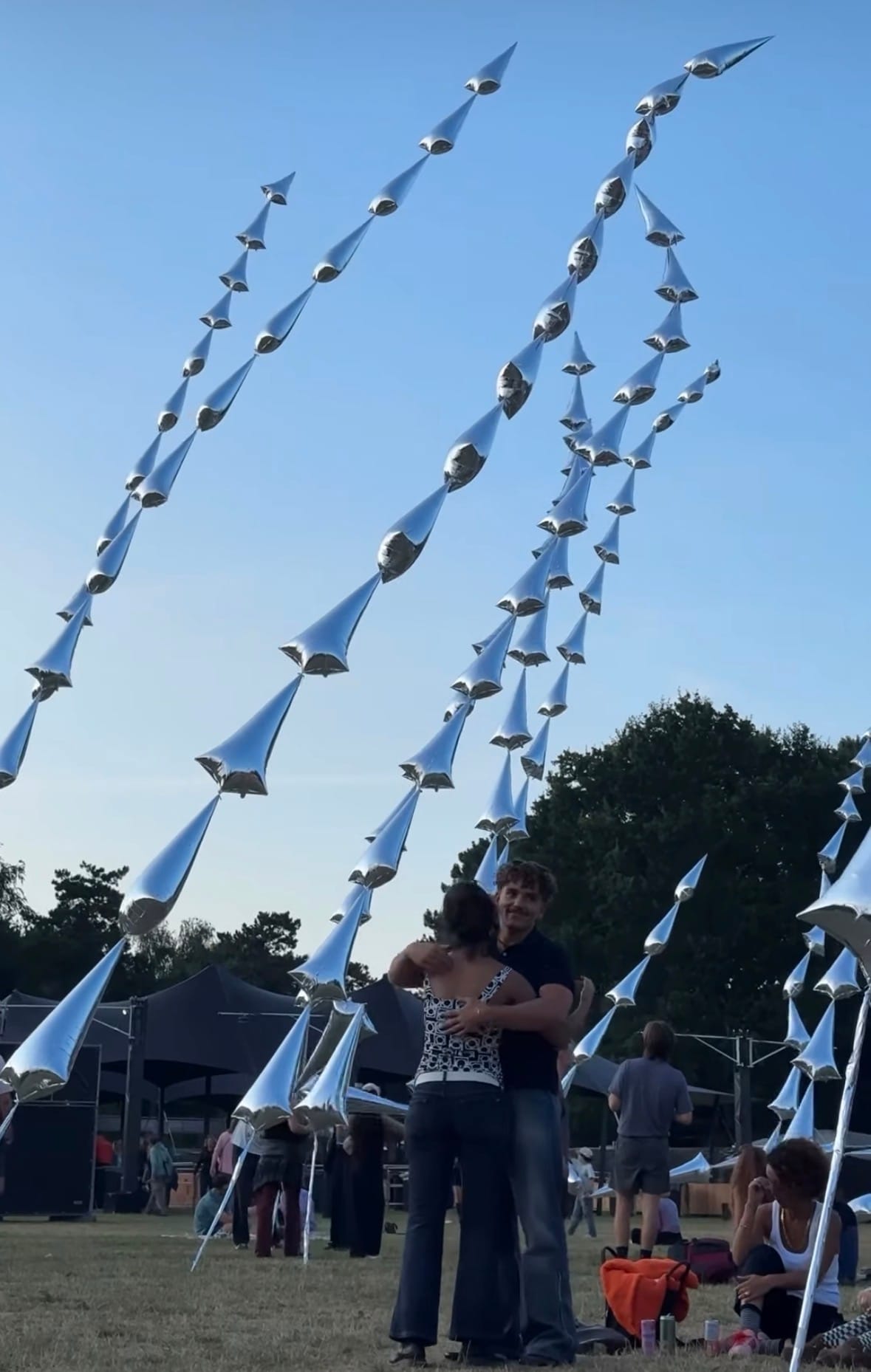 Bezoekers dansen bij zonsondergang tussen de zilverkleurige sculpturen van Steel Grass